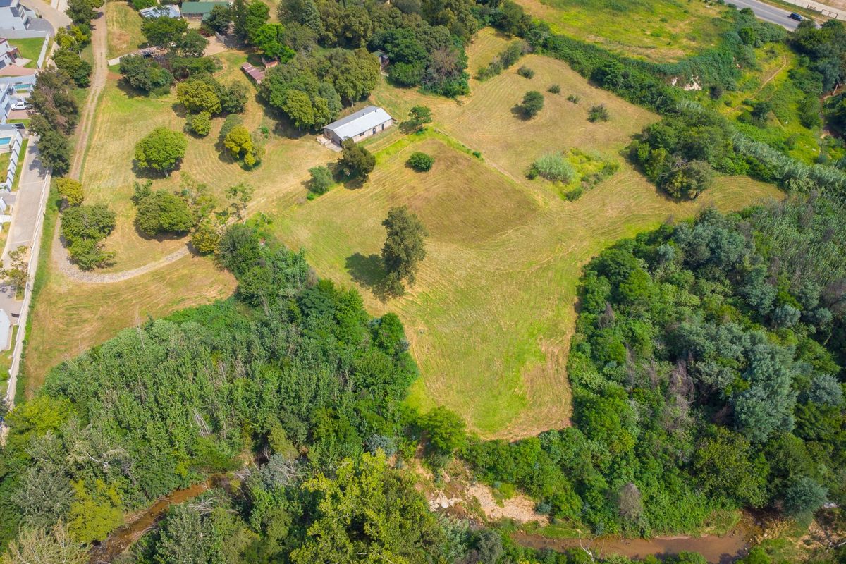An aerial view of a large small holding property featuring expansive green lawns, mature trees, and natural river frontage.