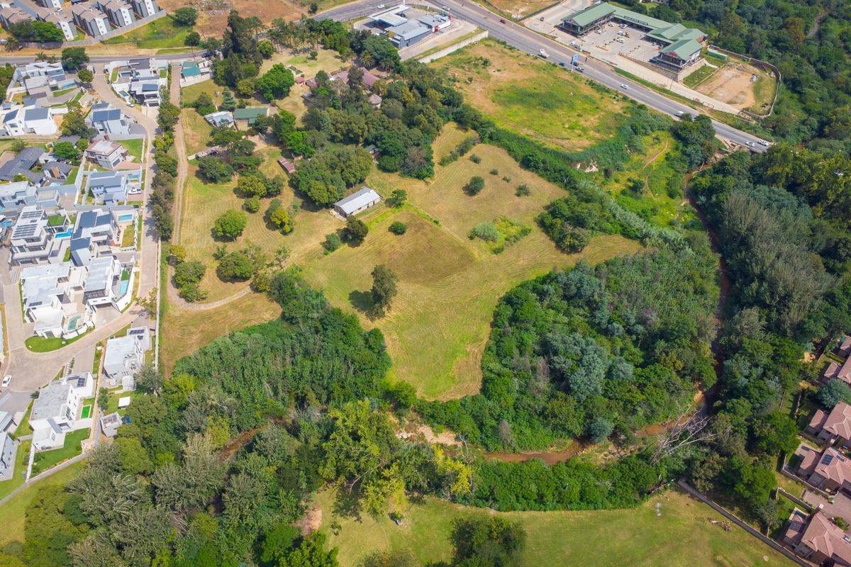 An aerial view of a large small holding property featuring extensive open land, mature trees, and natural river frontage bordering the site.