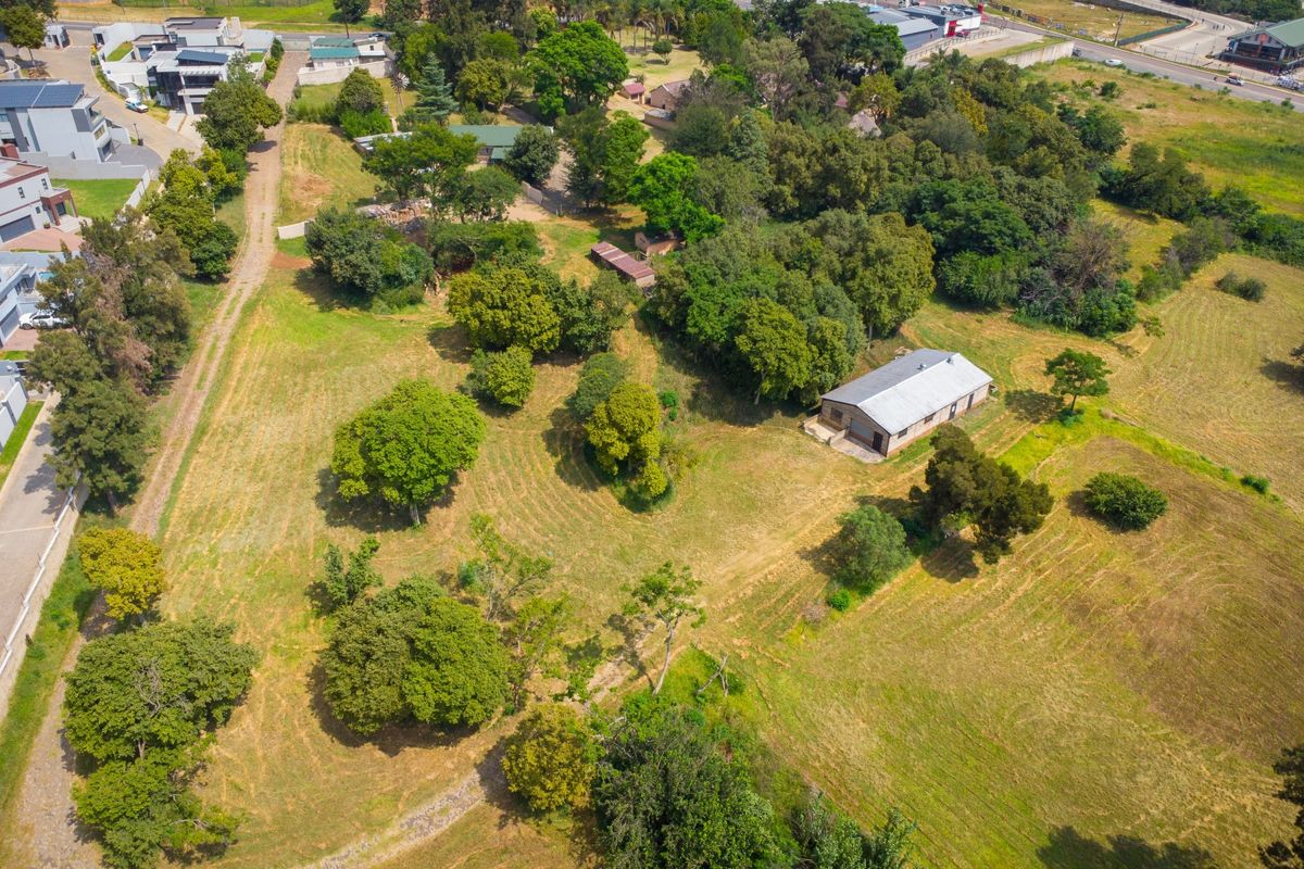 Aerial view of a spacious small holding property featuring mature trees, expansive grounds, and a single-story dwelling with a metal roof.