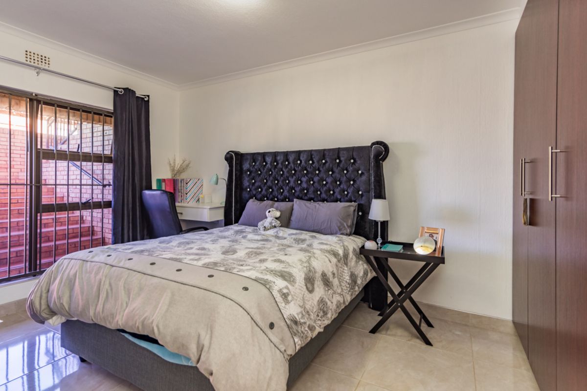A well-maintained bedroom featuring tiled flooring, a built-in wardrobe, and a sliding door with a security gate providing access to the exterior.