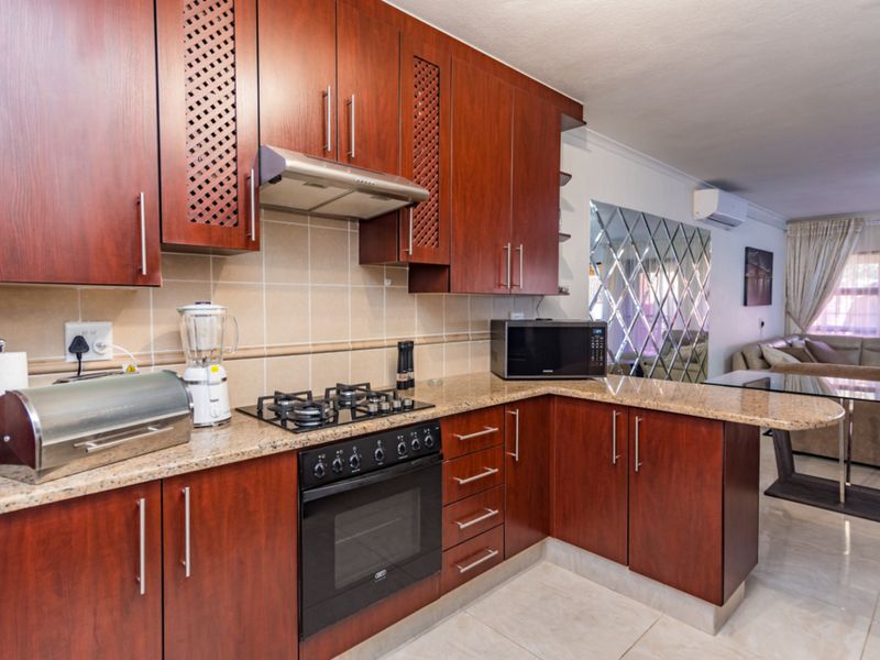 Open-plan kitchen featuring dark wood cabinetry, granite countertops, gas hob, and integrated oven, flowing into a living area with a decorative mirrored wall.