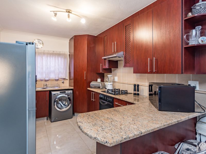 A functional kitchen featuring dark wood cabinetry, granite countertops, a gas hob, and integrated laundry space with tiled flooring.