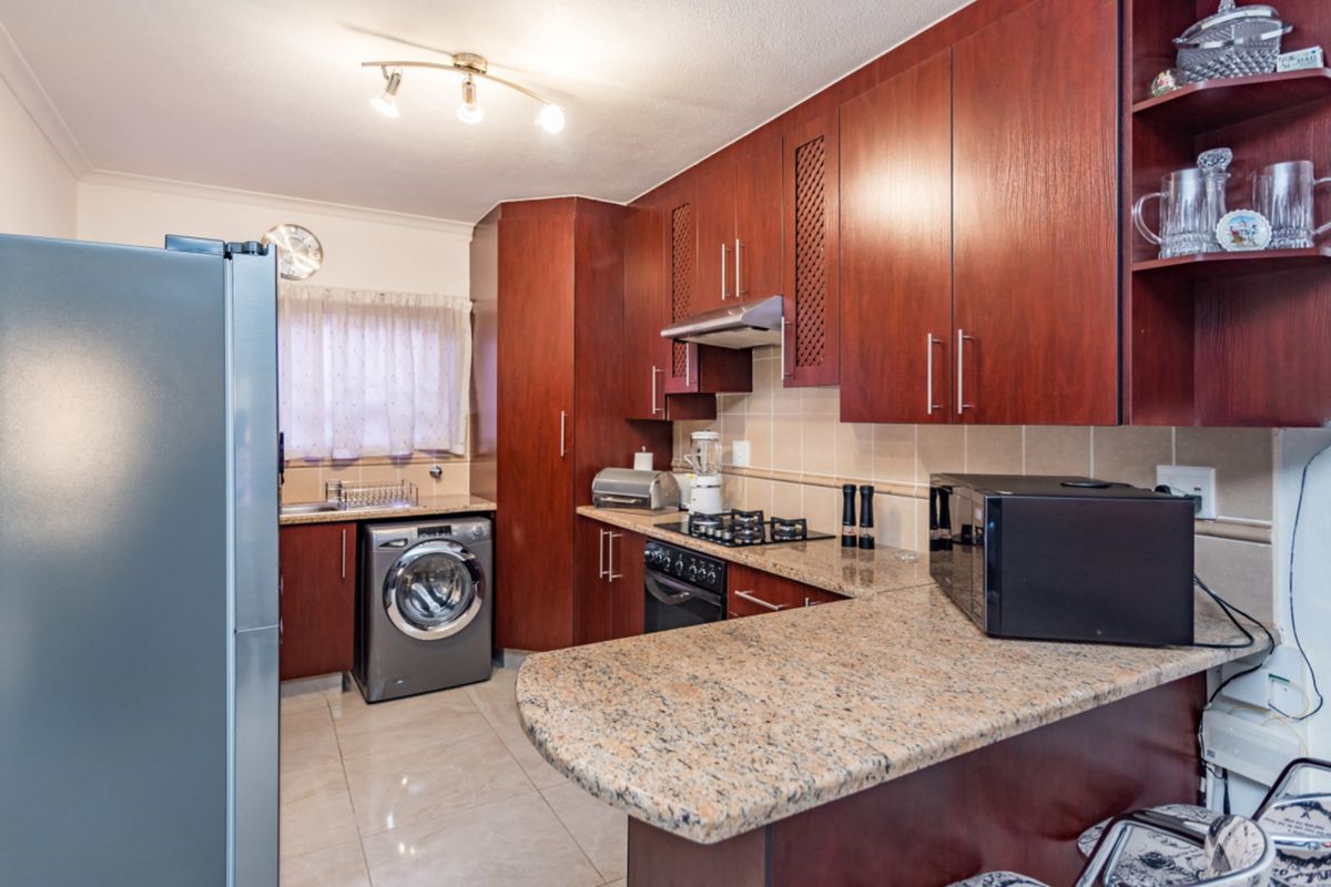 A functional kitchen featuring dark wood cabinetry, granite countertops, a gas hob, and integrated laundry space with tiled flooring.