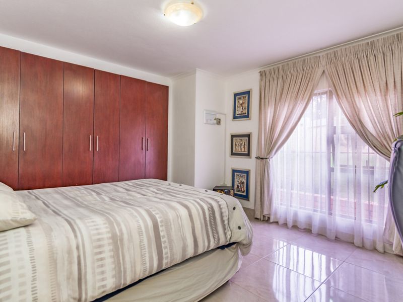 A bedroom featuring built-in wooden cupboards, tiled flooring, and a window with curtains providing natural light.