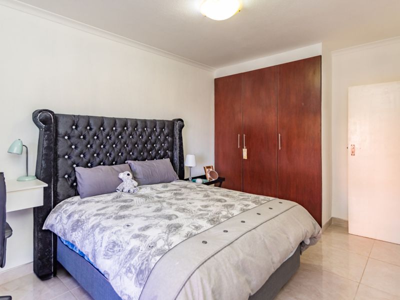 A bedroom featuring tiled flooring, a built-in wooden wardrobe, and a central ceiling light fixture.