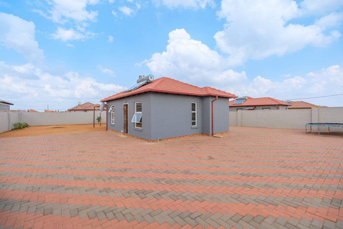 Rear view of a detached house featuring a paved yard, perimeter wall, and a solar water heating system installed on the tiled roof.