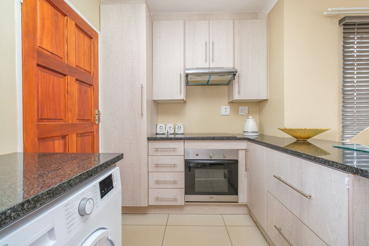 Compact kitchen featuring light wood-grain cabinetry, granite countertops, built-in oven and hob, extractor fan, and tiled flooring.