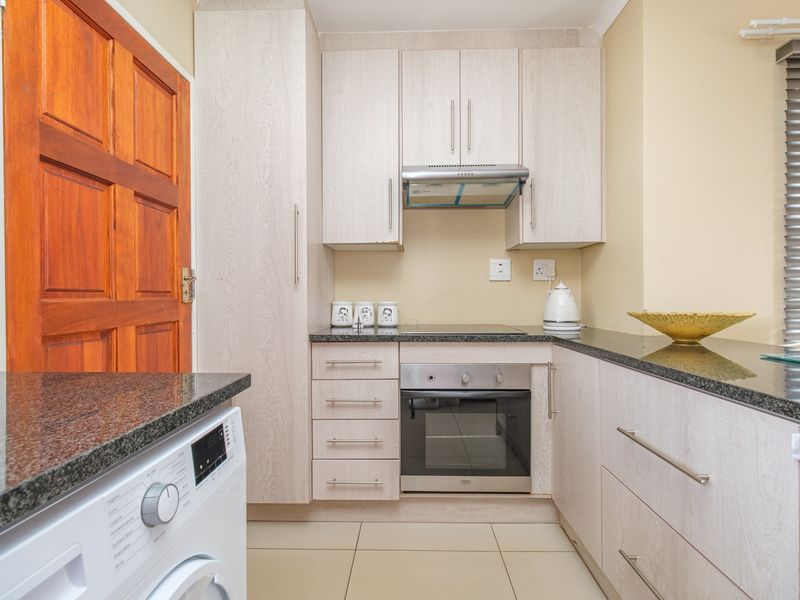 Compact kitchen featuring light wood-grain cabinetry, granite countertops, built-in oven and hob, extractor fan, and tiled flooring.