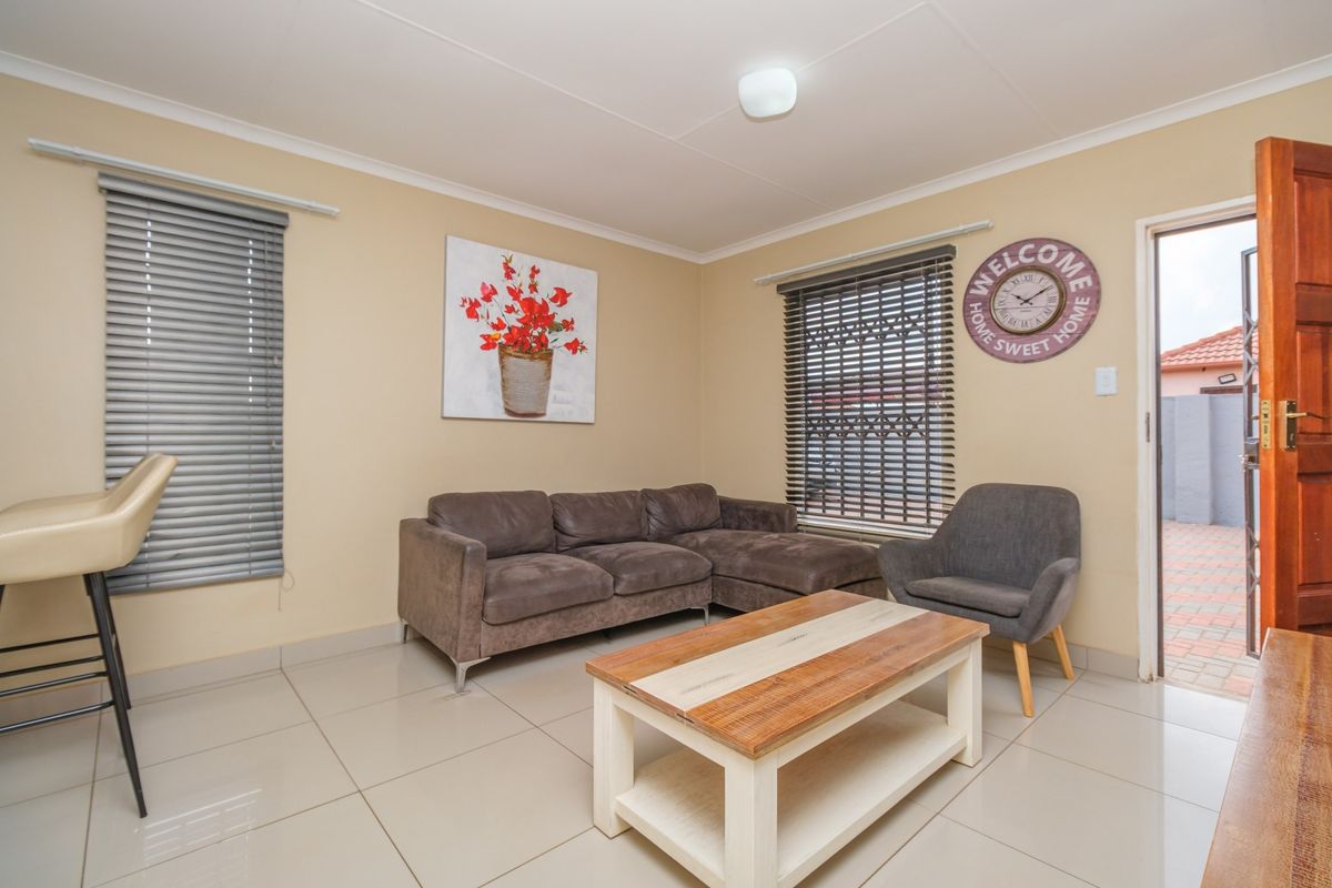A functional living room featuring neutral tiled flooring, venetian blinds, and direct access to an outdoor area through a wooden door.