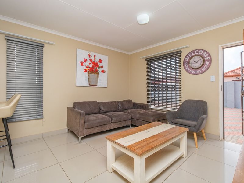 A functional living room featuring neutral tiled flooring, venetian blinds, and direct access to an outdoor area through a wooden door.