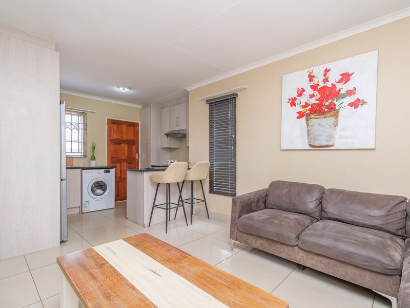 An open-plan living area featuring a compact kitchen with built-in cabinetry, a breakfast counter, and tiled flooring throughout.