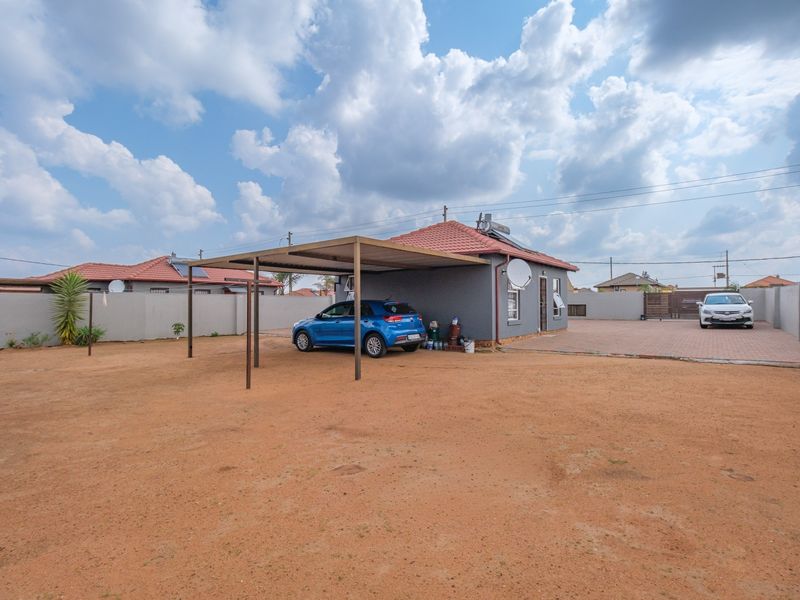 Front exterior view of a residential house featuring a carport, paved driveway, perimeter wall, and solar geyser installation.