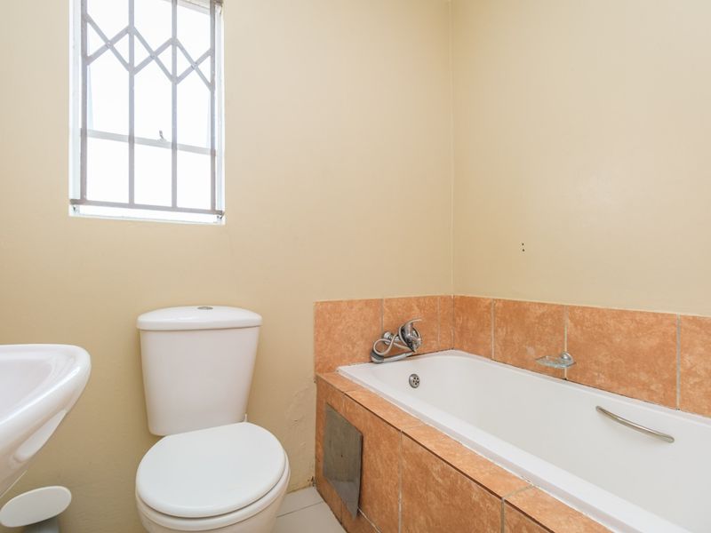 A functional bathroom featuring a bathtub with tiled surround, a standard toilet, and a pedestal basin, requiring minor cosmetic updates.