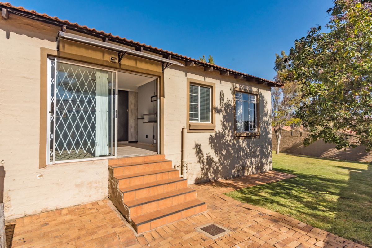 Rear exterior view of the townhouse featuring a brick paved patio, tiled steps leading to a sliding glass door, and established garden area.