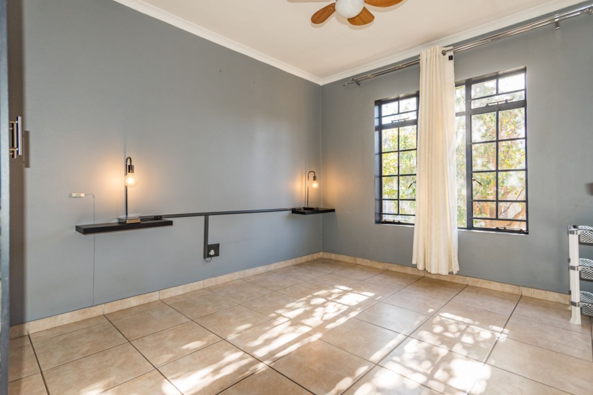 A bright, empty bedroom featuring tiled flooring, a ceiling fan, and wall-mounted shelving units with integrated lighting.