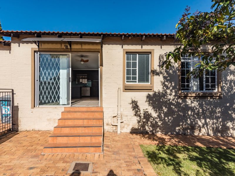 Rear exterior view of the townhouse featuring a brick paved patio, tiled entrance steps, and a sliding glass door with security gate.