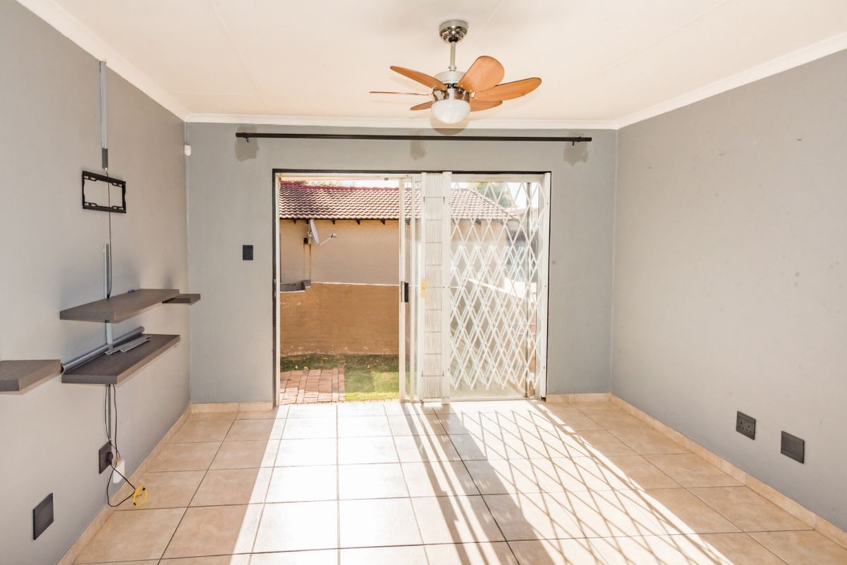 An empty living room featuring tiled floors, a ceiling fan, and a sliding glass door with a security gate leading to the rear exterior.
