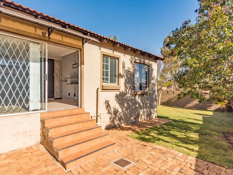 Rear exterior view of the townhouse featuring a brick paved patio, tiled entrance steps, and a sliding glass door with security gate.