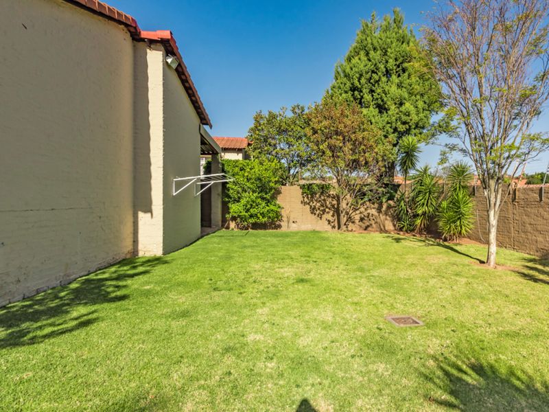 A private rear garden featuring a well-maintained lawn, perimeter brick boundary walls, and a wall-mounted clothesline attached to the townhouse structure.