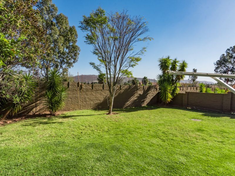 A well-maintained private garden featuring a lush green lawn, established trees, and a secure perimeter wall with electric fencing.