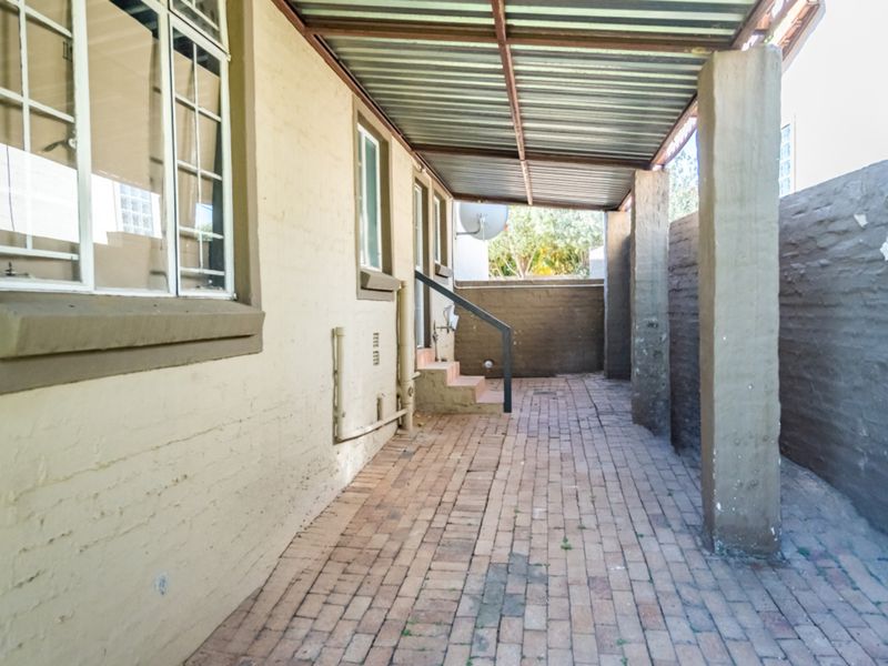 A covered outdoor patio area featuring brick paving, concrete columns, and a corrugated metal roof, providing a functional space for outdoor living.