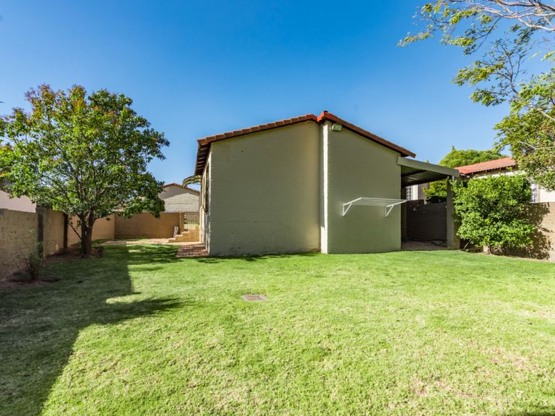 A spacious rear garden featuring a well-maintained lawn, brick boundary walls, and a covered patio area attached to the townhouse structure.