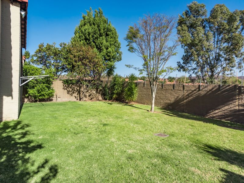 A private rear garden featuring a well-maintained lawn, perimeter wall with electric fencing, and a wall-mounted clothesline.