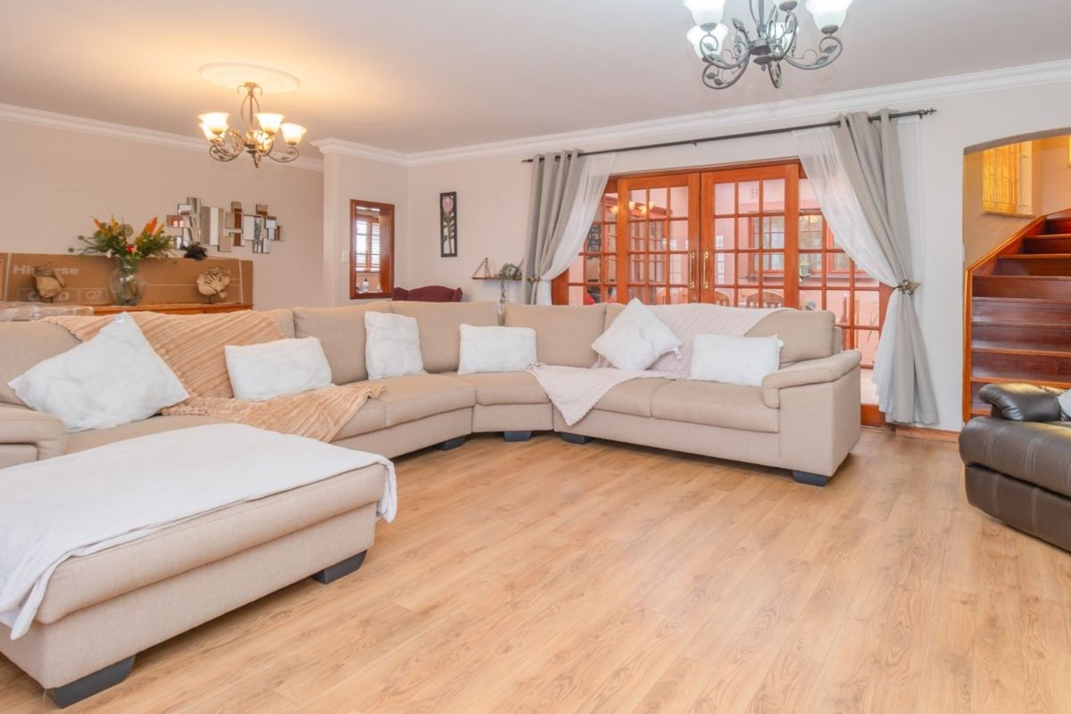 Spacious living room featuring laminate flooring, elegant chandeliers, ceiling roses, and direct access to the patio through wooden french doors.