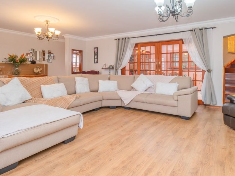 Spacious living room featuring laminate flooring, elegant chandeliers, ceiling roses, and direct access to the patio through wooden french doors.