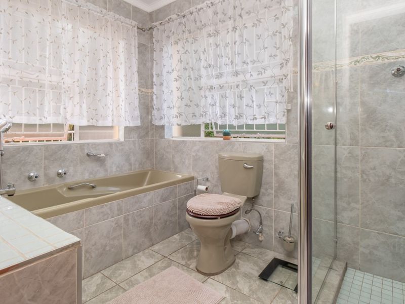 A functional bathroom featuring a built-in bathtub, separate glass-enclosed shower, and tiled finishes throughout.