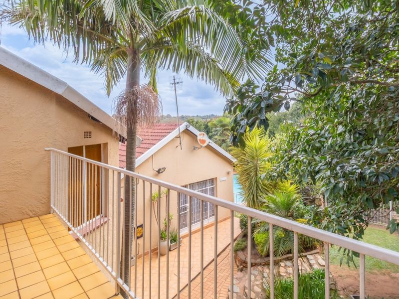 An elevated balcony with tiled flooring and metal railings, overlooking the rear garden and pool area of the property.