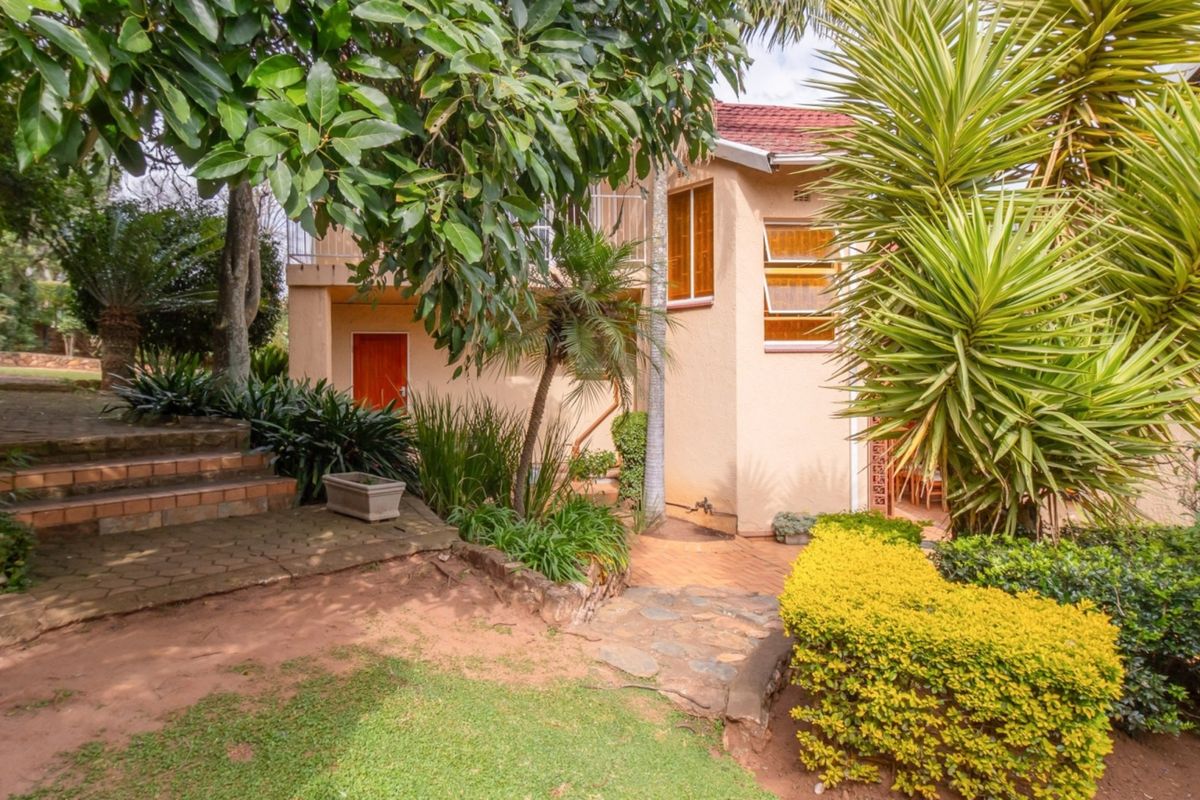 Rear exterior view of the property featuring a tiled roof, brick paved pathways, stone steps, and established garden landscaping.