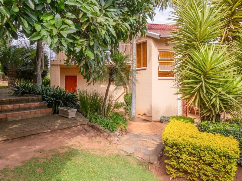 Rear exterior view of the property featuring a tiled roof, brick paved pathways, stone steps, and established garden landscaping.