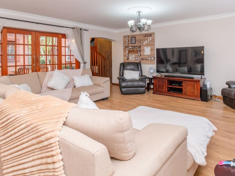 Spacious living room featuring laminate flooring, crown molding, and wooden french doors providing access to the outdoor area.
