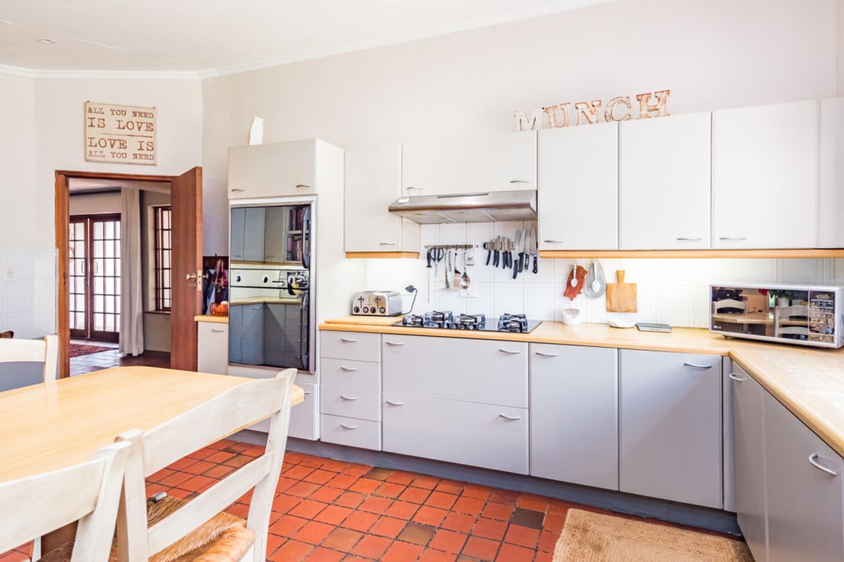 A functional kitchen featuring light-toned cabinetry, a gas hob with extractor fan, built-in oven, and traditional terracotta-style tiled flooring.