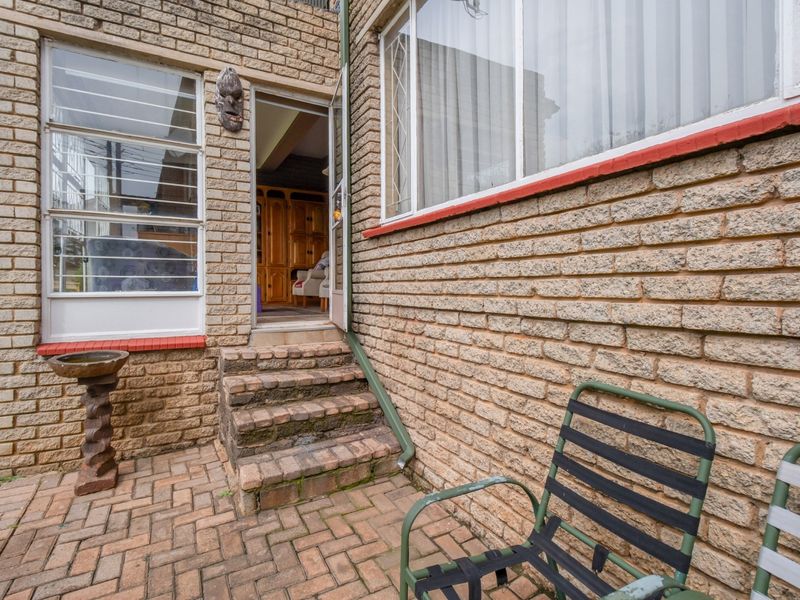 Rear exterior view of the apartment featuring a brick-paved patio area, brick facade, and access steps leading into the interior.