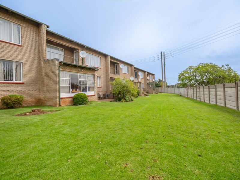 Rear view of a multi-story apartment complex featuring face brick construction, a large communal lawn, and secure boundary walling.