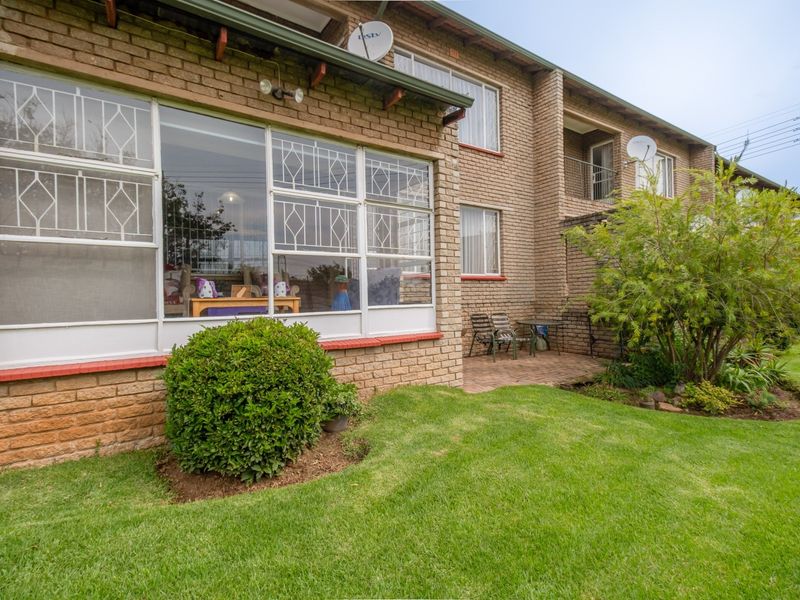 Rear view of the apartment building featuring a face brick facade, large steel-framed windows, and a paved patio area overlooking a private garden.
