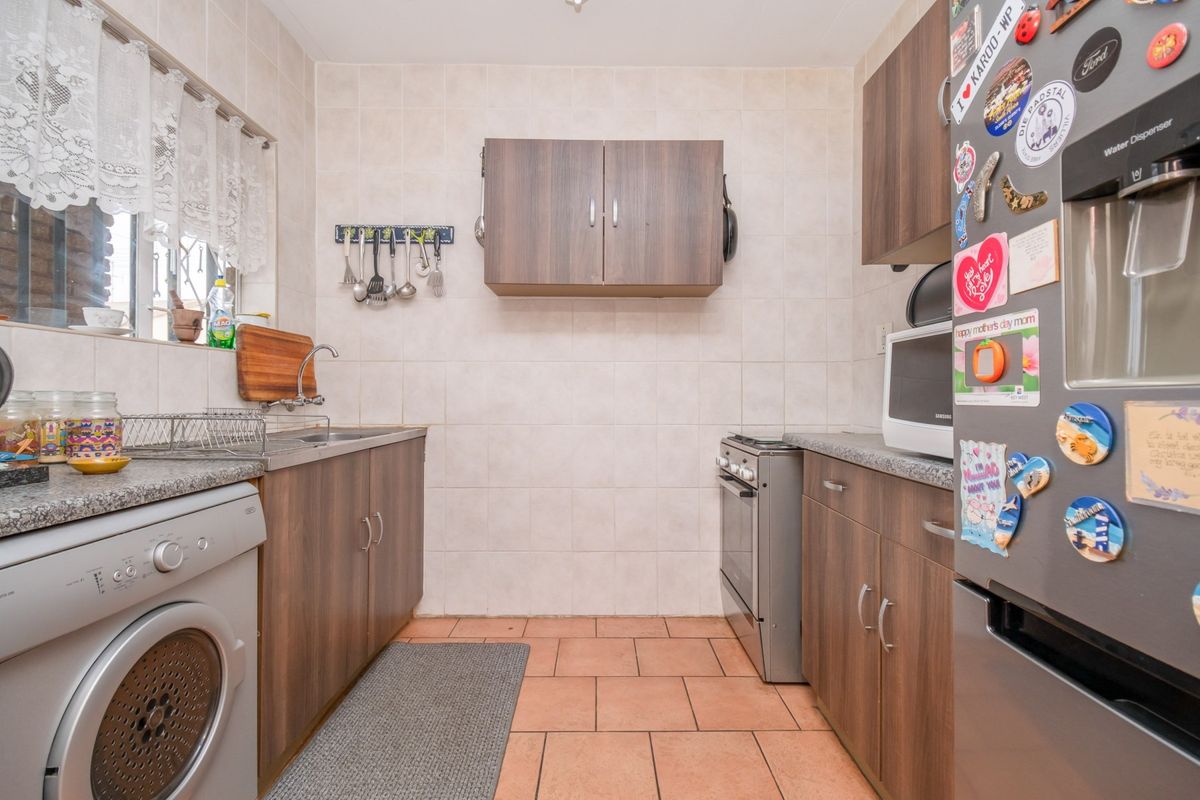 A functional kitchen featuring wood-finish cabinetry, granite countertops, tiled backsplash, and space for a washing machine and freestanding stove.