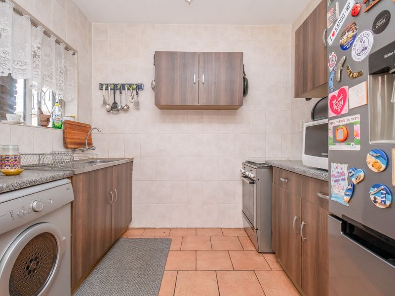 A functional kitchen featuring wood-finish cabinetry, granite countertops, tiled backsplash, and space for a washing machine and freestanding stove.