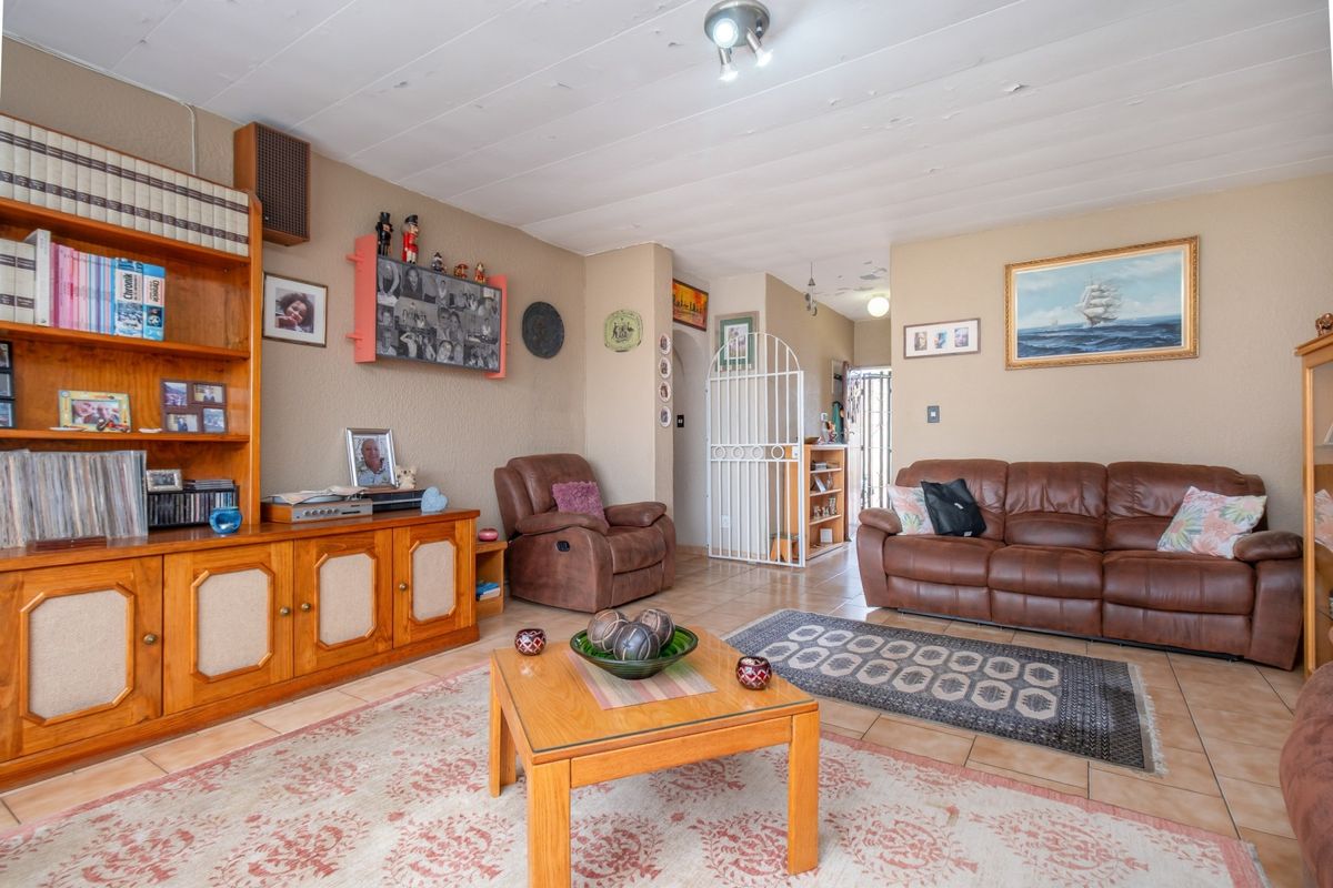 A living room featuring tiled flooring, a built-in wooden shelving unit, and a security gate leading to the entrance area.