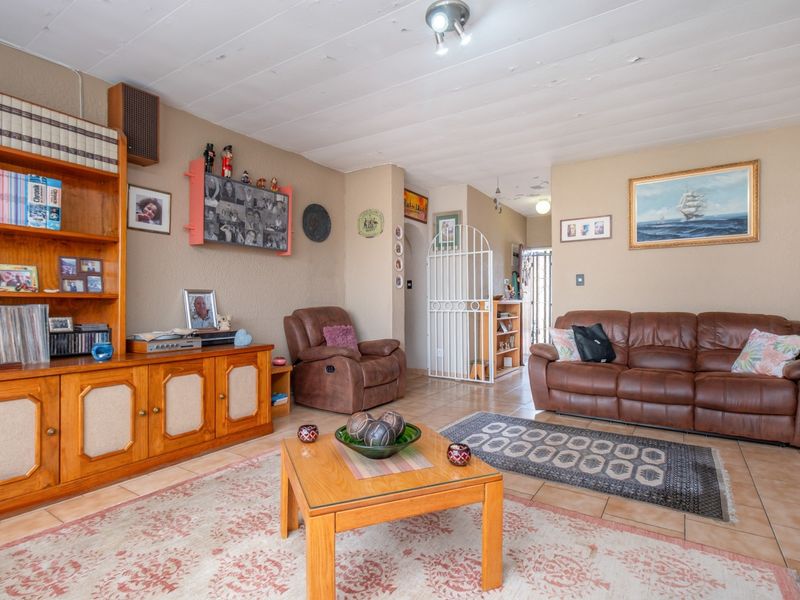 A living room featuring tiled flooring, a built-in wooden shelving unit, and a security gate leading to the entrance area.
