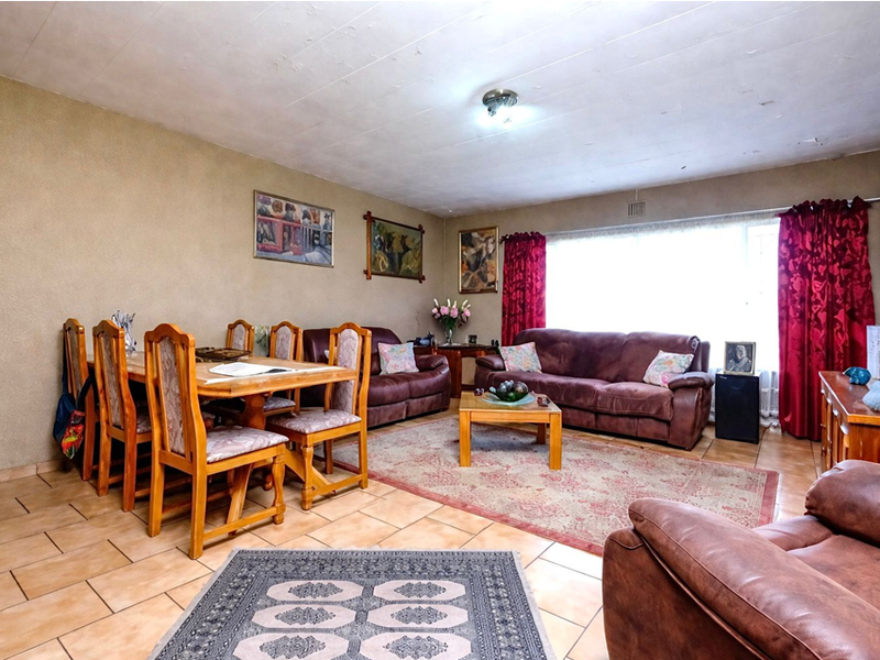 Open-plan living and dining area featuring tiled flooring, a large window for natural light, and a built-in wooden shelving unit.