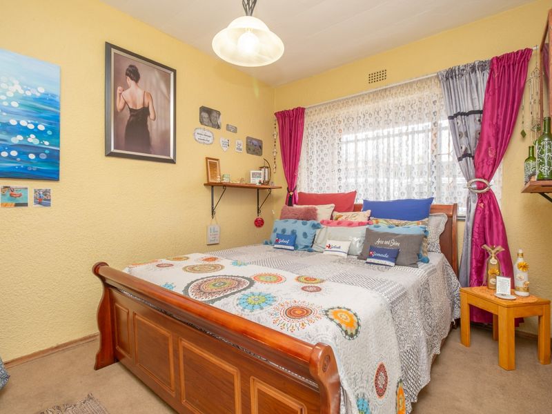 A cozy bedroom featuring yellow textured walls, a central ceiling light, and a ventilation grille above the window area.