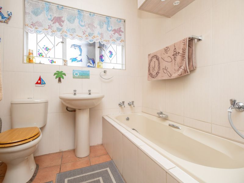 A functional bathroom featuring a pedestal basin, built-in bathtub, and toilet with neutral wall tiling and terracotta-style floor tiles.