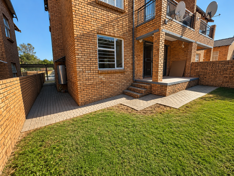 Rear view of a face brick apartment building featuring a paved patio area, small garden, and balcony with metal railings.