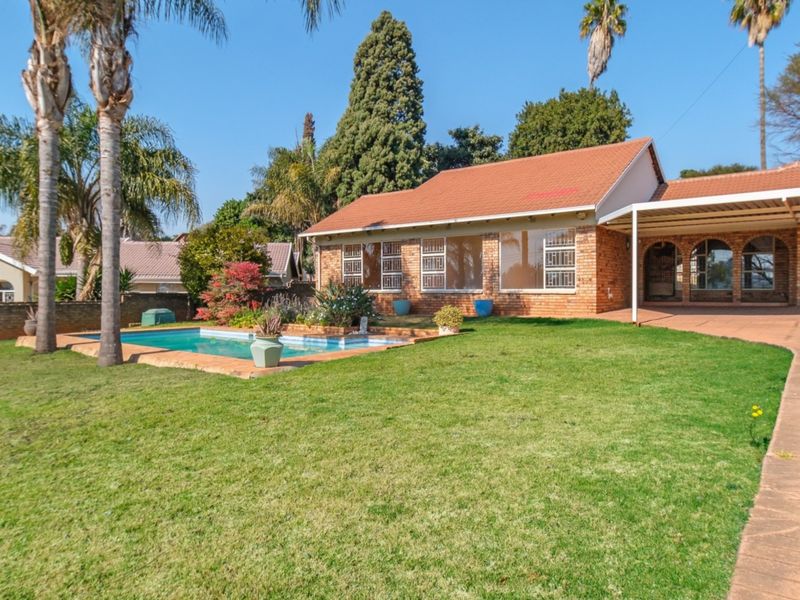 Rear view of the property featuring a brick facade, a swimming pool, a paved patio area, and a well-maintained garden.