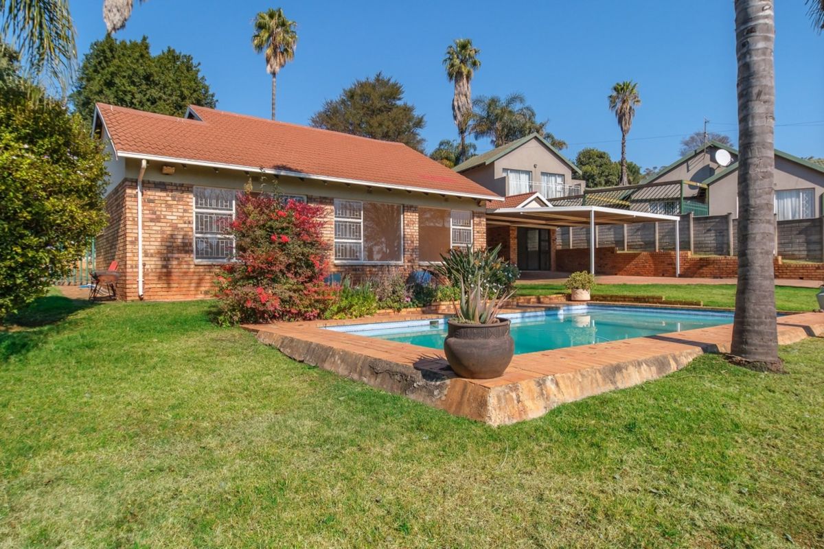 Rear view of the property featuring a brick house, a swimming pool with paved surround, a covered patio area, and a spacious garden.