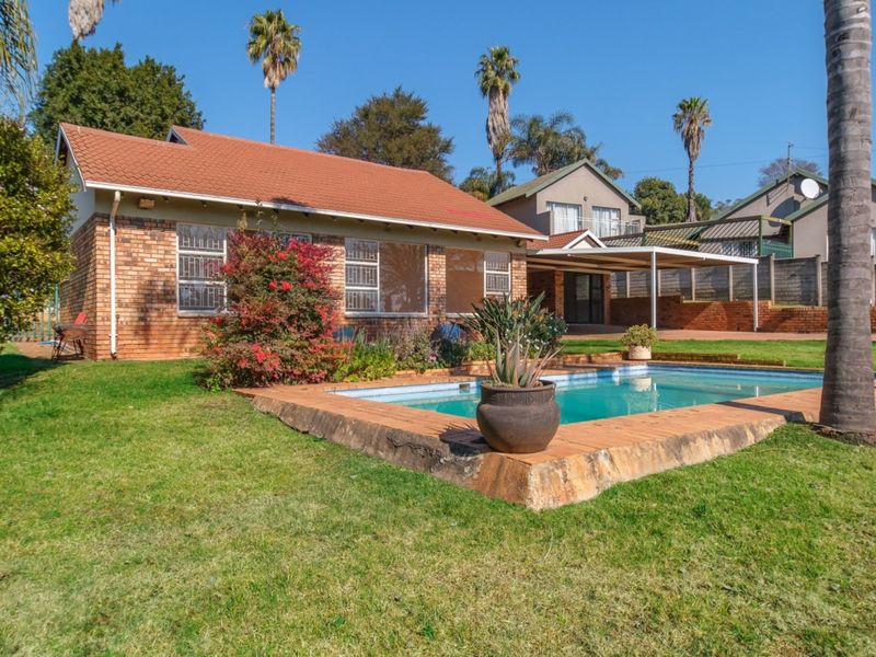 Rear view of the property featuring a brick house, a swimming pool with paved surround, a covered patio area, and a spacious garden.