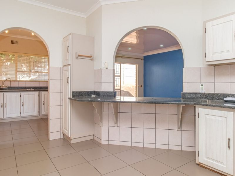 A functional kitchen featuring granite countertops, tiled splashbacks, and built-in cabinetry with a breakfast bar opening into an adjacent living space.